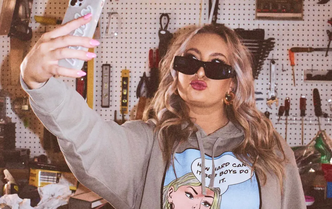 An image of Maddy Mitchell taking a selfie in her merch